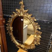 An ornate gilted oval wall hanging mirro