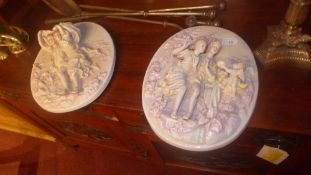 A pair of porcelain wall plaques with cherubs and maidens in relief