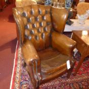 A pair of wing back armchairs upholstered in buttoned tan leather with brass studded detail and