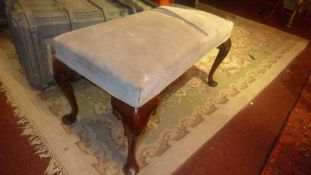 A mahogany footstool upholstered in grey suede and raised on cabriole supports