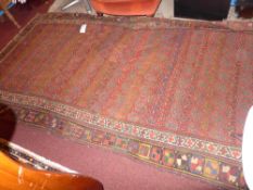 A hand made antique Persian carpet decorated with a repeating motif on a red field surrounded by two