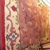 A Persian carpet with an ivory medallion on a terracotta field decorated with flowers surrounded