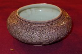 A Chinese squat form bowl with dragons flying over the sea in relief