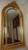 A wall mirror of large size with arched bevelled plate with ornately carved divisional gilt frame