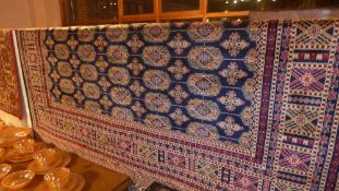 A Persian Bokhara style carpet the dark blue field with repeating motifs in gold in a triple border