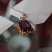 A yellow metal pendant with inset amythyst stone