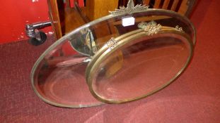 An Art Deco looking glass with oval bevelled plate and a similar brass framed mirror [2]