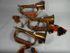 Three copper and brass bugles with decorative bound tassles and two bearing Regimental badges of the