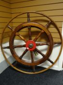 A large wooden ship's wheel with painted red and brass fitting, 4 feet in diameter