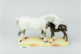 A Beswick pottery model of a dappled grey mare with her foal standing on a green and light brown