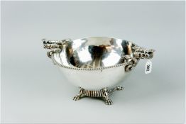 A beaten silver bowl on a short pedestal with four substantial claw supports and handles in the form