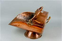An antique copper helmet coal scuttle with swing handle and a circular raised base