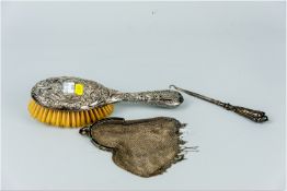 An oval silver backed dressing brush, a silver handled button hook and a white metal, possibly