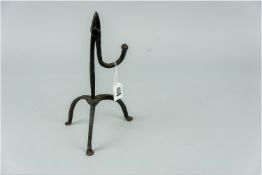 A wrought iron rush light holder having a single hook shaped nip, standing on a three legged base,