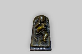 A large cold painted bronze figure of a reclining baby upon a cushion eating grapes and holding