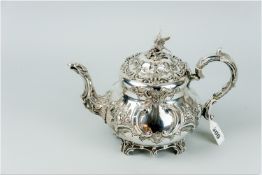 A circular Rococo style silver teapot with raised flowers and scrolls and with hinged lid having