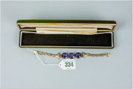A believed nine carat gold bracelet of dark shaped links and three large round cut purple stones,