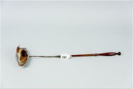 A silver ladle with long turned wooden handle, the ladle itself having a tapered silver handle of