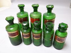 Four ribbed green glass pharmaceutical bottles all with red and gold labels, 8 ins high (20 cms)