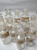 Fifteen clear glass pharmaceutical bottles with stoppers, all with white chemical labels with red