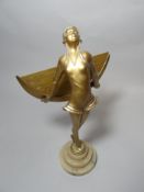An Art Deco standing metallic figure of a lady in swimwear holding a crescent shaped glass disc,