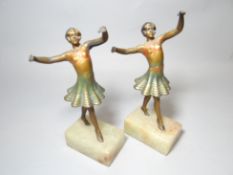 A pair of painted metallic Art Deco dancing girl figures on marble block bases, 9 ins high (23 cms)