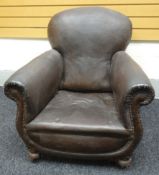 A brown leatherette studded club armchair on bun-feet with casters