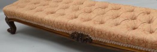 A Victorian walnut framed long foot-stool with buttoned stuff-over upholstery and carved frieze,
