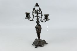 A cast bronze twin sconce candelabra of a young person semi-robed standing upon a three footed