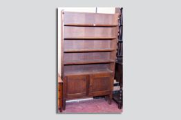 A circa 1930s oak bookcase of five open shelves with twin cupboard doors below on block supports, 72