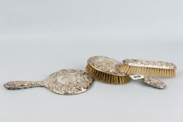 A silver backed circular dressing mirror and two brushes