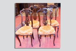 A set of four late 19th/early 20th Century mahogany dining chairs having carved swept  top rails