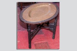 An Indian carved oval table and stand with dished oval brass tray, decorated with multi panels of
