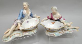 Pair of sweetmeat dishes in the form of a reclining man and lady on scrolling gaudy bases, blue-