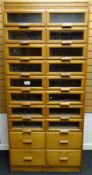A late twentieth century light wood retailer's haberdashery cabinet with two columns of eight glazed