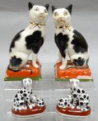 A pair of porcelain black and white seated cats on red and green cushion bases, 7.5 ins high (19