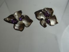 A pair of silver floral earrings set with two pear amethysts to each