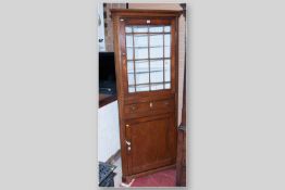 A provincial oak one piece standing corner cupboard with sixteen panel glazed top door over a single