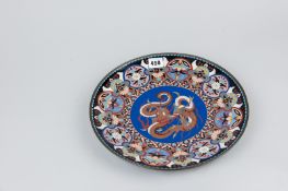 An Oriental cloisonne plate with central swirling dragon decoration on a blue ground and repeating