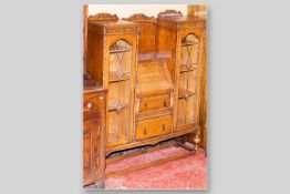 An early 20th Century carved oak side by side bureau bookcase with leaded glass doors on bulbous