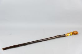 A carved wooden walking stick, the shaft with snakeskin cover, the top with a carved figure of a man