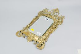 A 19th Century ornate brass framed wall mirror with bevelled edge glass, 16 x 9 ins (40.5 x 23 cms)