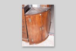 A Georgian oak two door bow fronted hanging wall cupboard with eagle crest, pierced brass