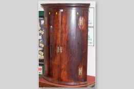 A Georgian mahogany bow front two door wall cupboard with brass 'H' hinges and escutcheons, the