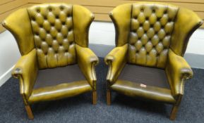 A pair of distressed brown leather button and studded wing-back library armchairs