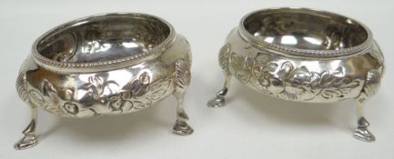 A pair of cauldron shaped silver salts on raised pad-feet and with embossed flowers to the body,