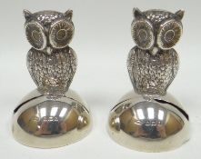 A pair of silver menu holders in the form of perched owls, feather decorated and upon semi-