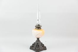 An iron based oil lamp with yellow tinted milk glass reservoir and chimney