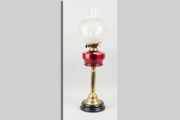A brass based oil lamp with cranberry glass reservoir and etched bowl shade