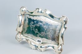 An oblong bright cut silver dressing table tray with shaped border and a panel to the base of floral